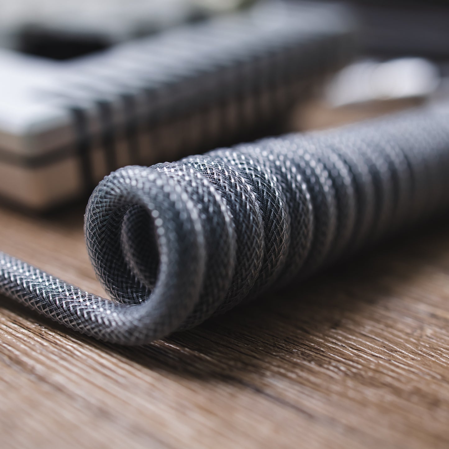 Closeup of sleeved cable coil. Teleios carbon grey/gray, TechFlex Clear, FEMO 1B push/pull connector, and bundled cable of the same type.